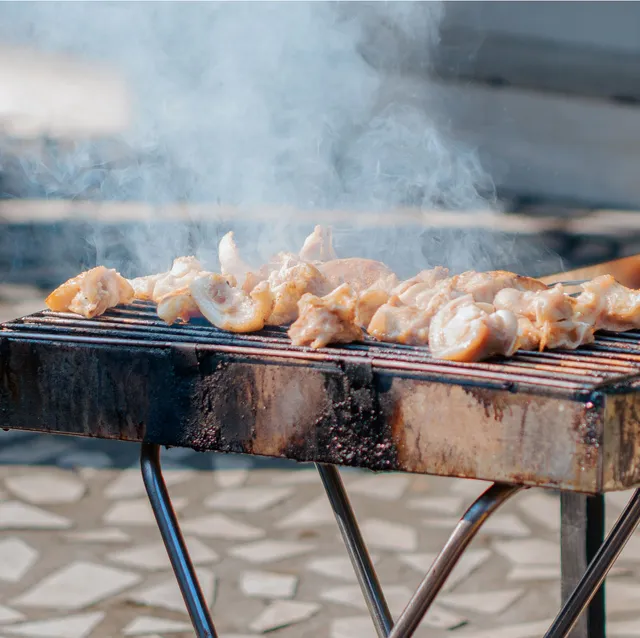 Chicken pieces smoking over an outdoor charcoal grill